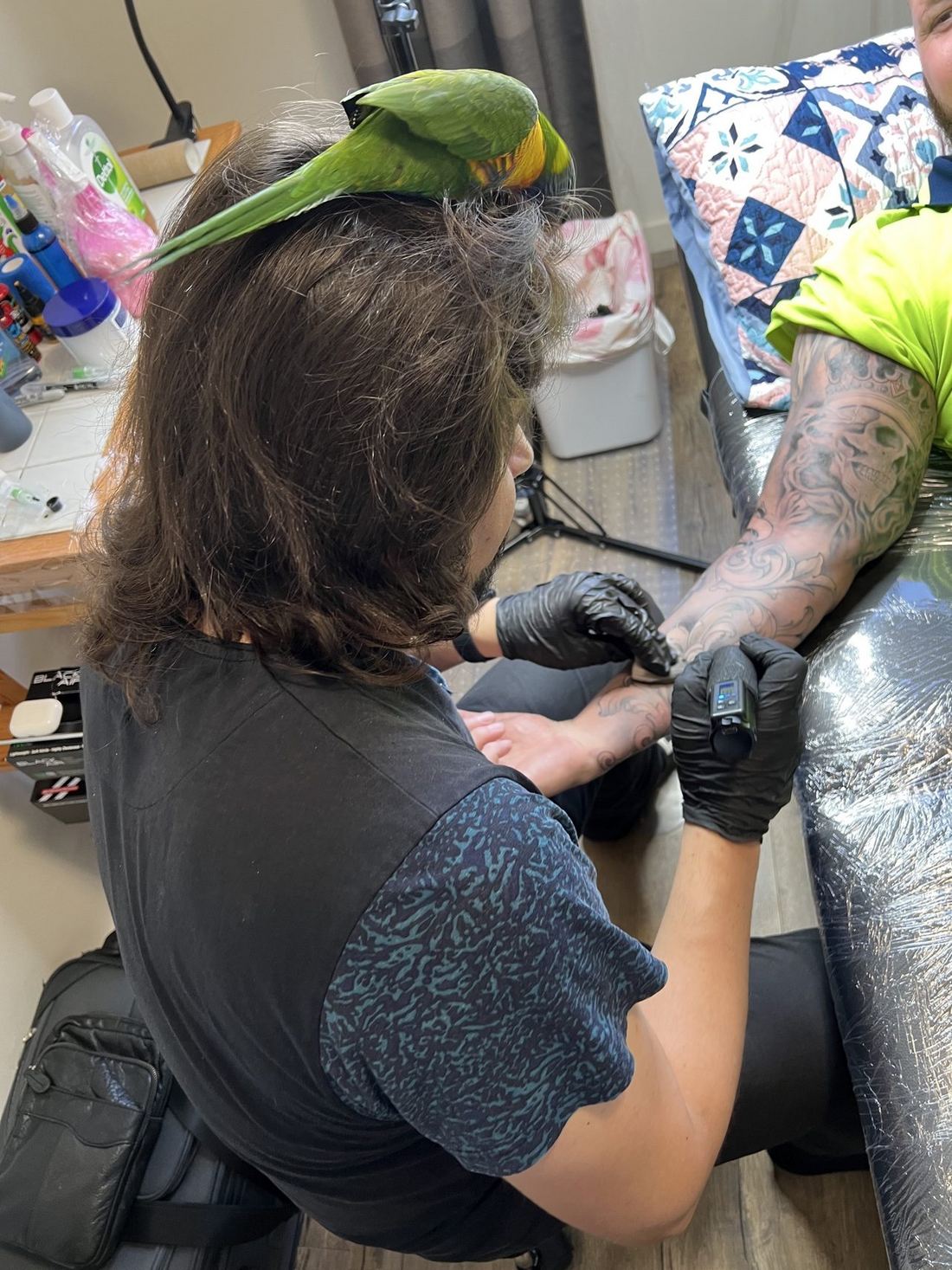 Scheklein Oleksandr tattooing with a parrot perched on his head